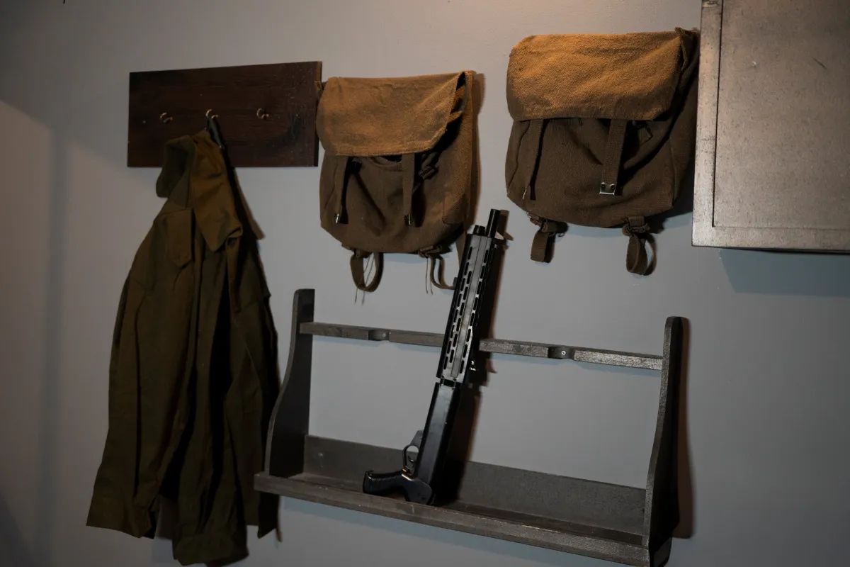 Requisiten im Escape Room Top Secret: Gewehr, Rucksäcke und Mantel an der Wand