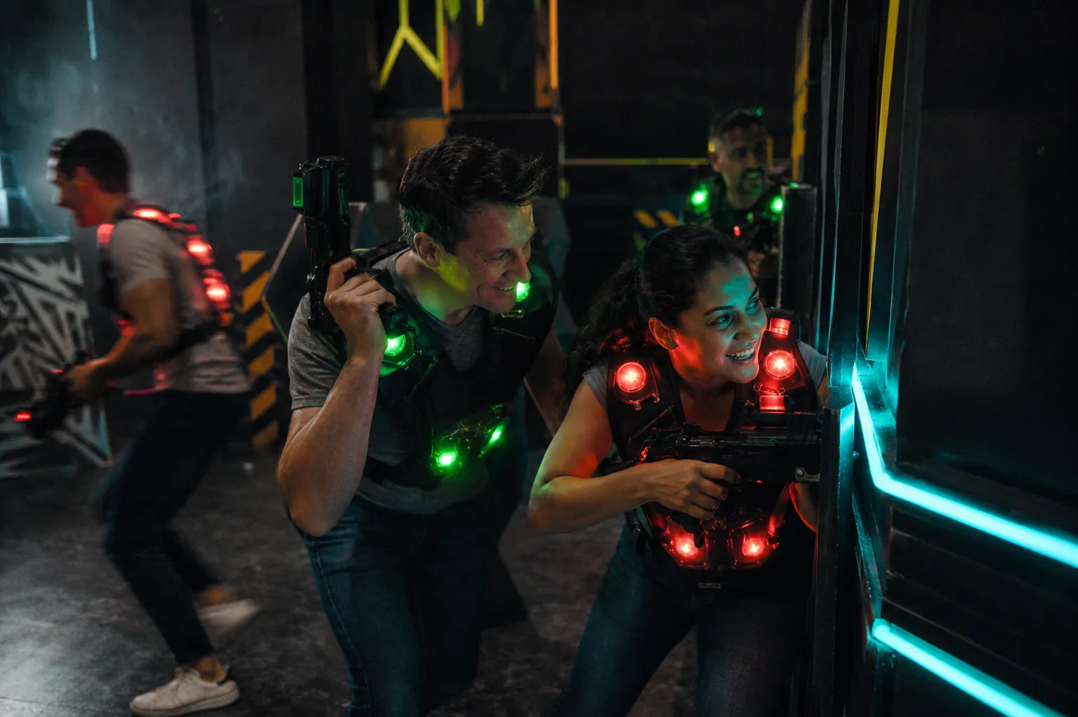 Kollegen mit leuchtenden Lasertag-Westen in Aktion in der dunklen Arena