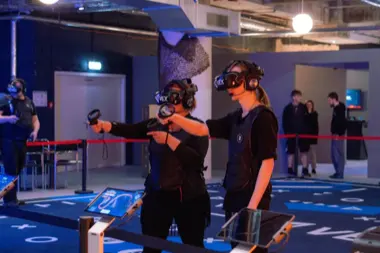Zwei Personen mit VR-Headsets, Controllern und taktilen Westen